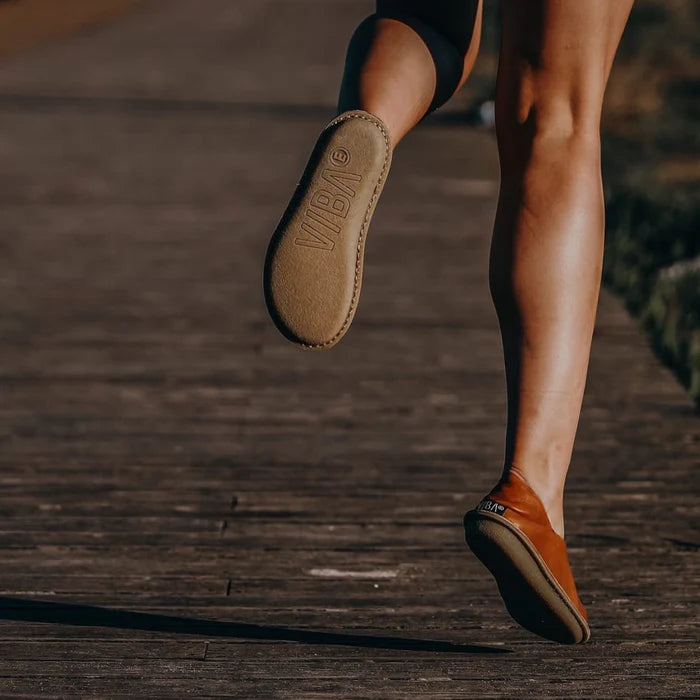Person springer på träspång i skor från VIBAe – närbild bakifrån med fokus på den tunna, flexibla sulan med VIBA®-logga